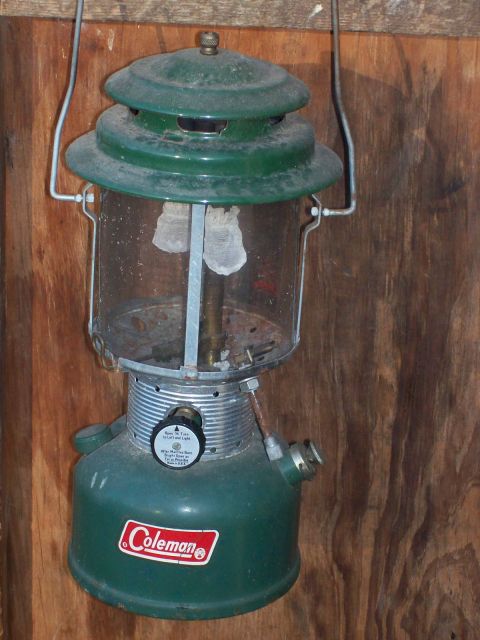 1982 Ford F-100 - A green Coleman lantern hangs against a wooden background. The lantern has a glass globe and two mantles inside.