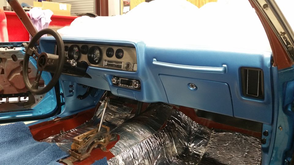 Interior of a classic car with blue dashboard, black steering wheel, and manual shifter.