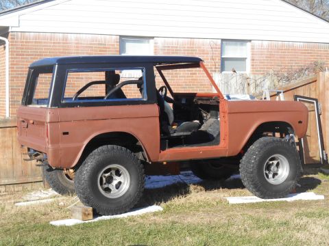 1972 Ford Bronco - The side profile of a vintage Ford Bronco undergoing restoration. The vehicle is brown with a black hardtop and has had its doors removed.