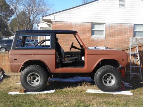 1972 Ford Bronco - A brown 1972 Ford Bronco is parked in a grassy yard next to a brick house. The vehicle has its doors removed and appears to be undergoing r…