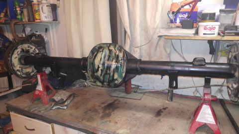1991 Ford Bronco - A black painted rear axle assembly with a camouflage-patterned differential cover is supported by red jack stands on a workbench. Various a…