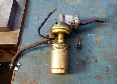 1964 Mercury Monterey - A mechanical fuel pump with attached hoses and a separate bolt sits on a workbench.