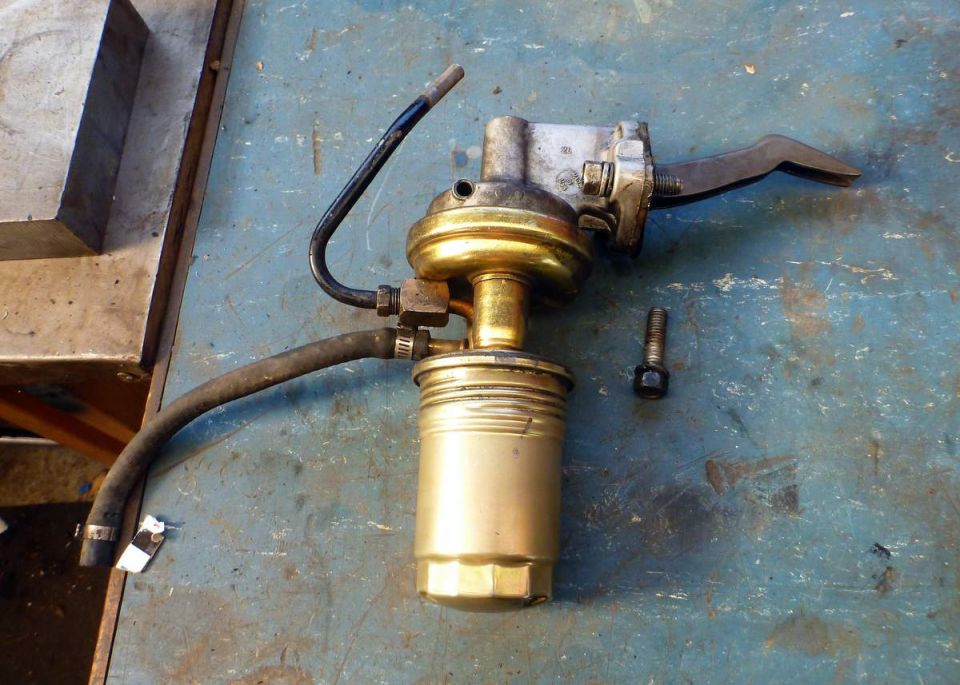 Gold and silver mechanical fuel pump with black hoses and a bolt on a blue surface