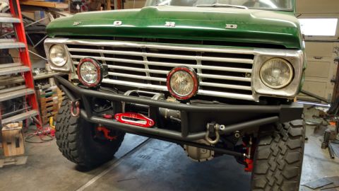 1967 Ford F-250 - The front grille and headlights of a green Ford truck are visible, equipped with a heavy-duty bumper and winch.