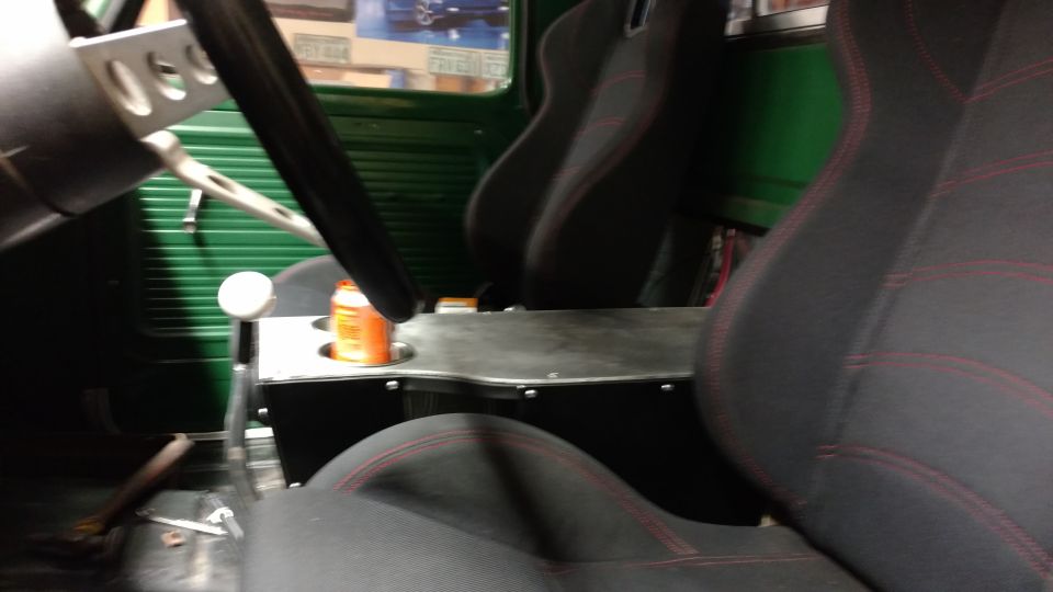 Interior shot of a truck with racing seats, a custom center console with a cup holder, and a steering wheel. Green ribbed door panels are visible