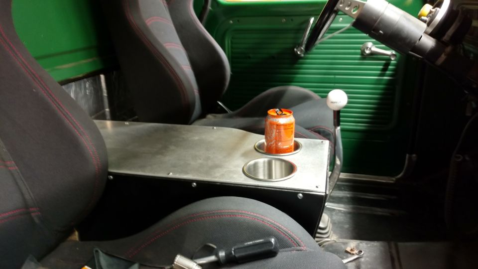 Green truck interior with bucket seats, custom center console with cup holders, and a white shift knob. An orange soda can sits in a cup holder