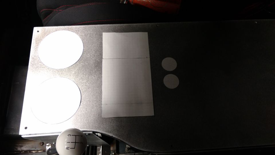 Metal dashboard panel with two large circles, a taped rectangle, and two small circles; gear shift visible below