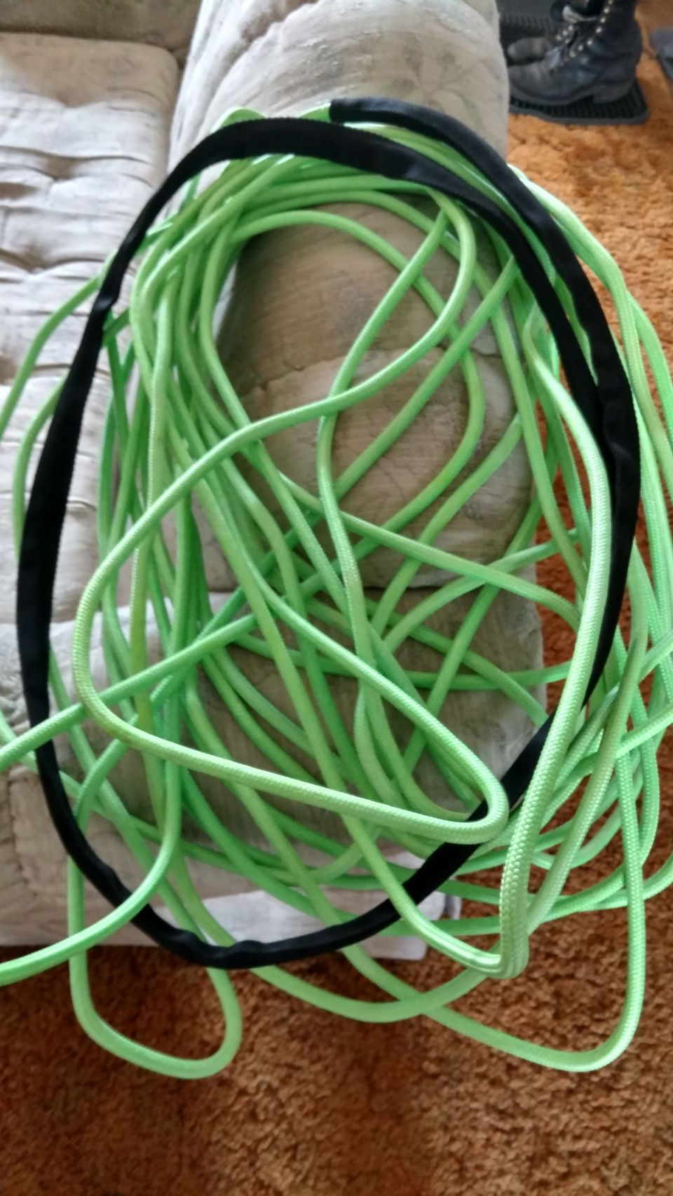 Tangled neon green rope with two black straps coiled on a couch and brown carpet