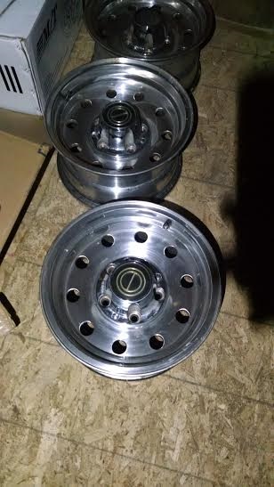 1994 Ford Bronco - A set of aluminum wheels are stacked on a wooden floor, with a box in the background.