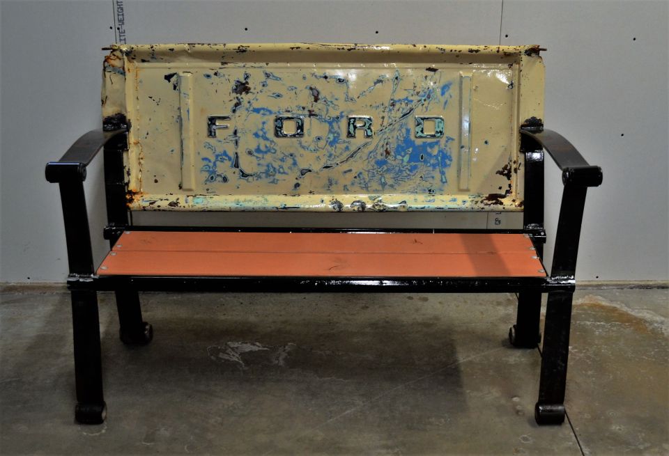 Bench with black metal frame and orange wooden seat, using a distressed yellow Ford tailgate as the backrest