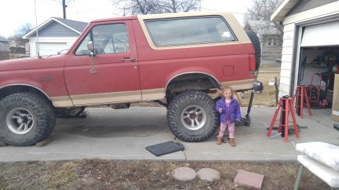 1991 Ford Bronco - A red 1991 Ford Bronco with a tan removable top is parked outside a garage.