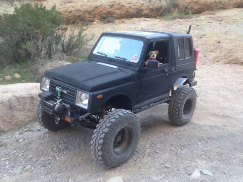 1987 Suzuki Samurai - A modified black Suzuki Samurai with a dog behind the wheel is parked on a rocky, dirt path.