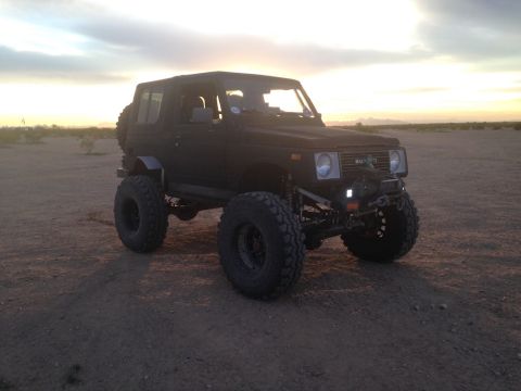 1987 Suzuki Samurai - A modified 1987 Suzuki Samurai sits in a dusty, arid environment as the sun sets behind it.