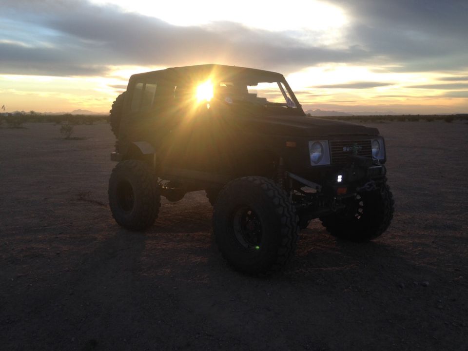 1987 Suzuki Samurai lifted with large tires, parked in a desert landscape at sunset