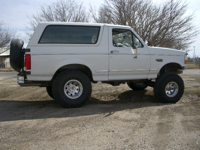 White 1994 Ford Bronco lifted with large tires, spare tire mounted on rear door