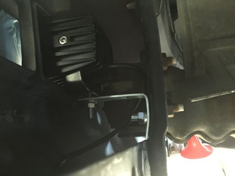 1996 Ford Bronco - Close-up view of an aftermarket fog light being installed on the underside of a vehicle, showing the mounting hardware.