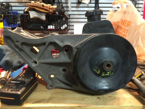 1996 Ford Bronco - A power steering pump bracket with yellow markings is shown on a workbench.