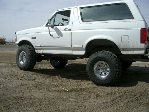 1994 Ford Bronco - This lifted white Ford Bronco SUV is shown from a side angle, with aftermarket wheels and tires.