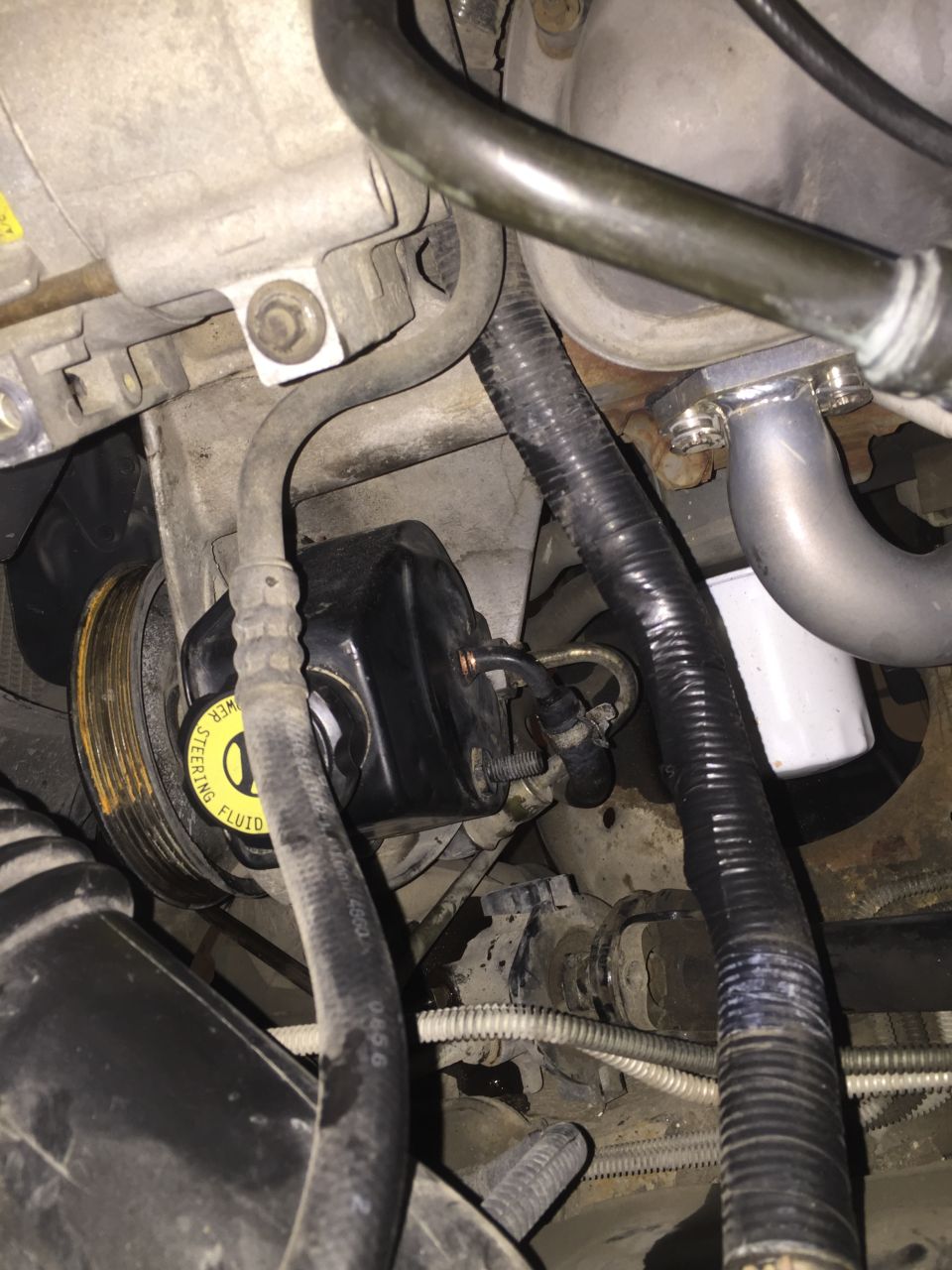 Power steering pump with yellow cap labeled 'POWER STEERING FLUID' and pulley