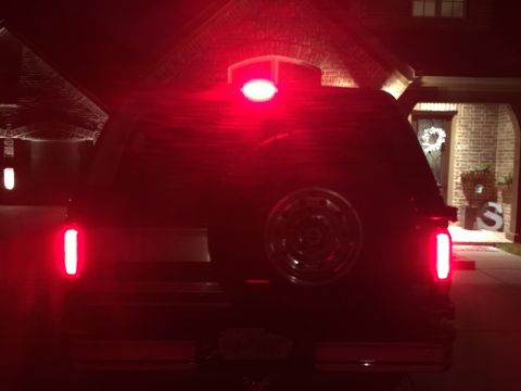 1996 Ford Bronco - The rear of a dark-colored SUV is illuminated by its red taillights and a third brake light.