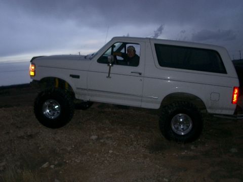 1994 Ford Bronco - A white SUV with a driver is parked on uneven terrain under a dusky sky.