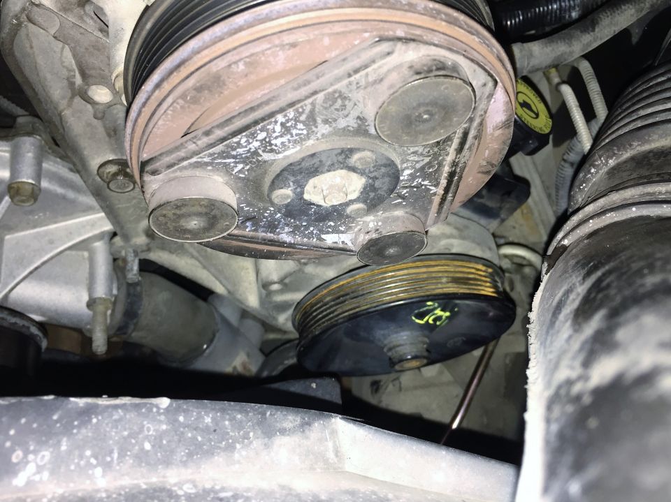 Engine pulley system with multiple belts and pulleys, showing wear and some white residue