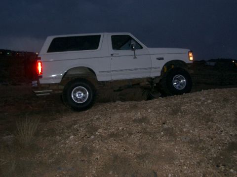 1994 Ford Bronco - A white 1994 Ford Bronco is shown in profile, lifted and driving on rough terrain at dusk.