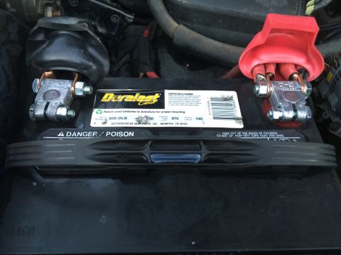 1996 Ford Bronco - Close-up of a car battery's positive and negative terminals with protective covers.