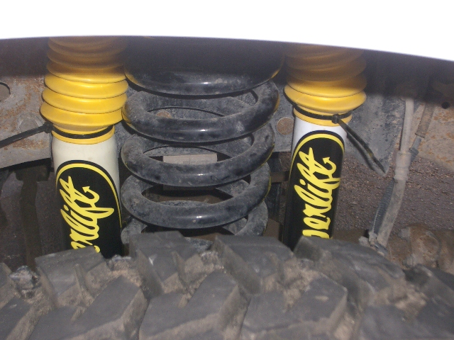 Close-up of yellow and white shock absorbers with 'Superlift' branding, next to a coil spring and tire tread
