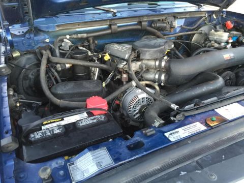 1996 Ford Bronco - Engine bay of a blue vehicle, showing various components like the battery and alternator.