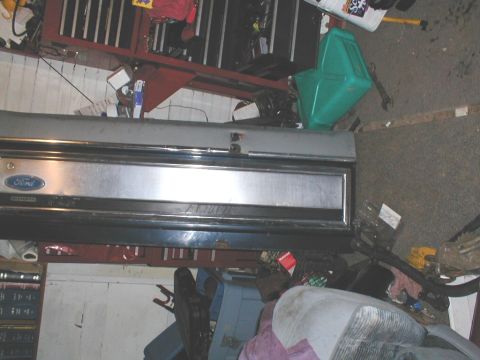 1979 Ford Bronco II - A Ford tailgate with chrome trim and emblem is visible, surrounded by various items in a cluttered space.