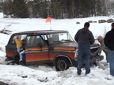 1979 Ford Bronco - Passenger-side view of a stripped, primer-black full-size Bronco with faded orange and yellow sunburst stripes down the body, doors removed…