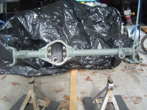 1986 Ford Bronco - A differential axle housing is shown, covered in black plastic sheeting and resting on wooden supports.