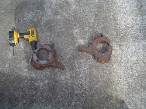1986 Ford Bronco - Two rusty steering knuckles and a yellow power drill lie on a concrete surface.