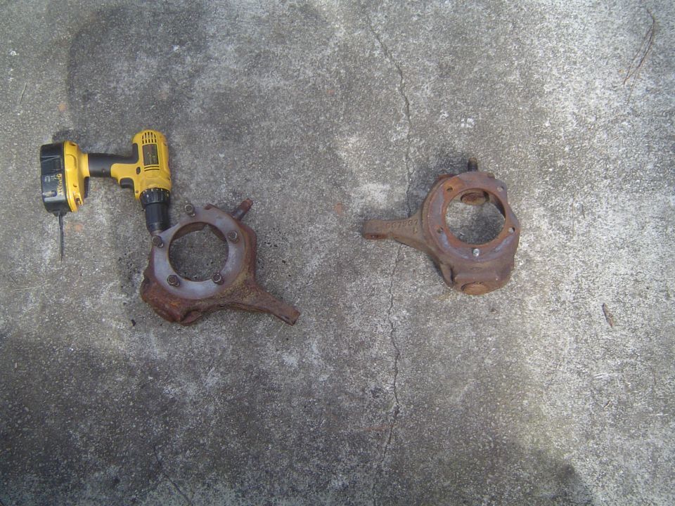 Two rusty steering knuckles and a yellow power drill on concrete