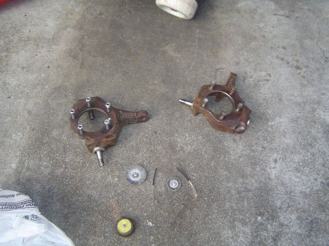 1986 Ford Bronco - Disassembled steering knuckles and associated parts laid out on a concrete surface.