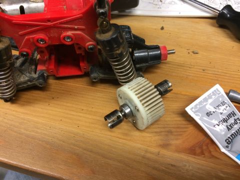 1989 Ford Bronco - Close-up of a disassembled RC car differential gear assembly, showing the gear, drive shafts, and part of the red chassis.