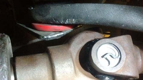 1985 Ford Bronco - Close-up view of a vehicle's driveshaft universal joint and a red suspension component.