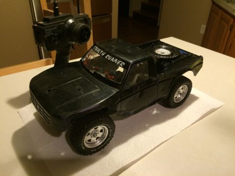 1989 Ford Bronco - A black remote control truck sits on a paper towel next to its controller, with a spare tire mounted in the bed.