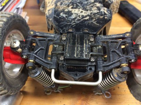 1989 Ford Bronco - The rear suspension and wheel assembly of a dirty RC car is shown, featuring black plastic suspension arms, silver coilover shocks, and a s…