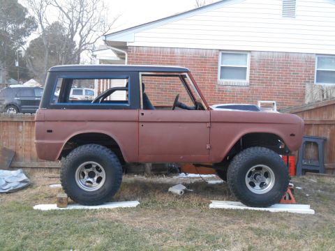 1972 Ford Bronco - A rusty, red 1972 Ford Bronco is parked on a grassy lawn in front of a brick house. The vehicle appears to be undergoing restoration, with…
