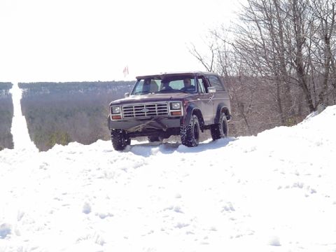 1979 Ford Bronco - A maroon Ford Bronco navigates a snow-covered incline on a bright, clear day.