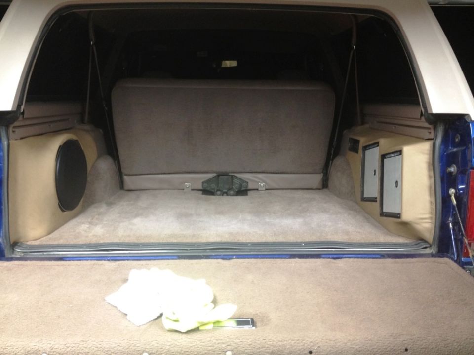 Interior cargo area of a blue SUV with custom tan speaker enclosures and subwoofer.
