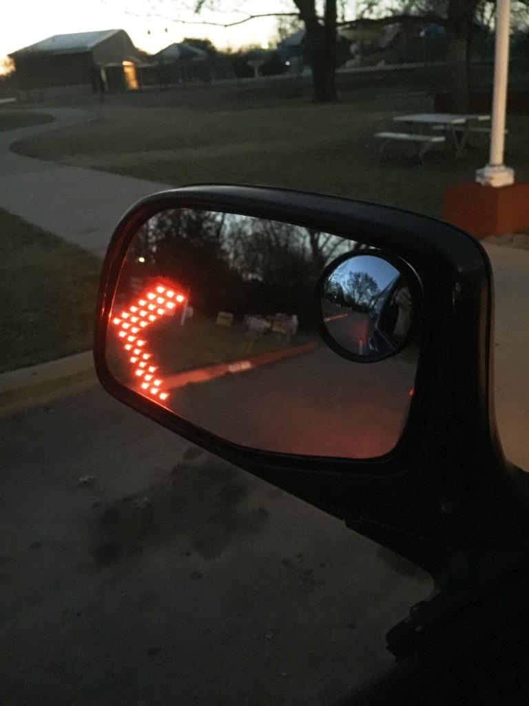 Side mirror with red arrow reflection and a smaller convex mirror.