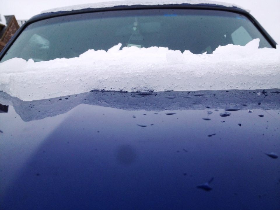 Melting snow and ice on the hood and windshield of a dark blue vehicle.