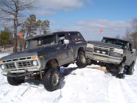 1979 Ford Bronco - Two Ford Broncos navigate a snowy terrain, one with a lifted suspension and aggressive tires.