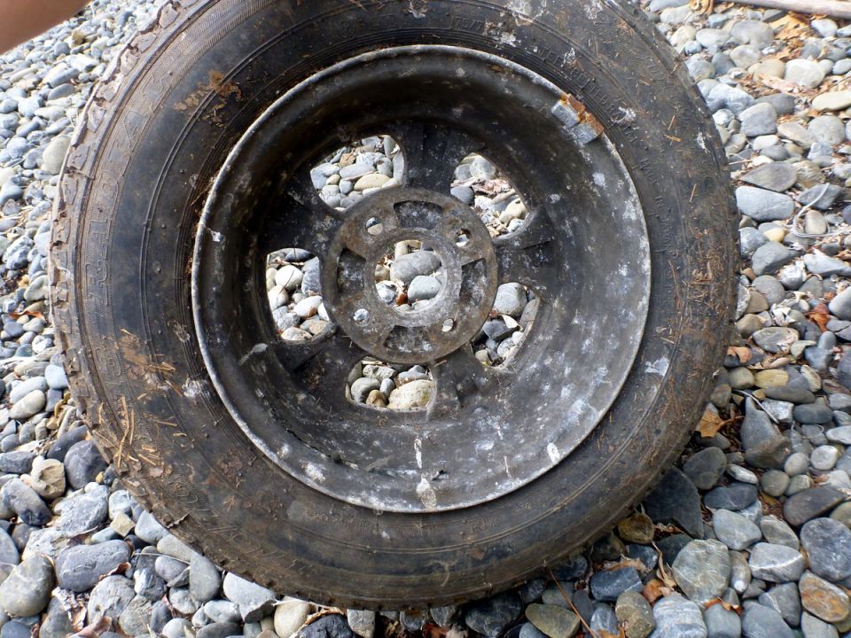 Overhead view of a dirty tire and rim on a rocky surface.