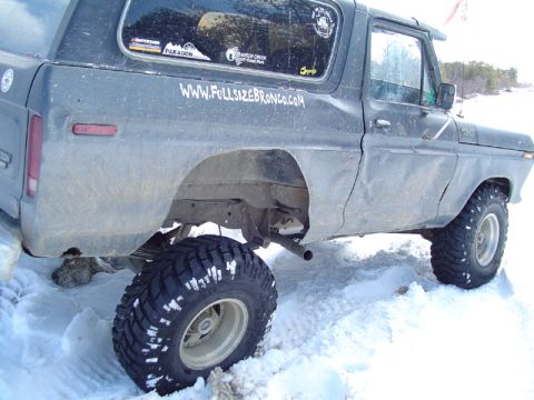1979 Ford Bronco - Low passenger-side view of a dark blue full-size Ford Bronco in the snow with cut-out rear fenders, a doorless cab, side-exit exhaust behin…
