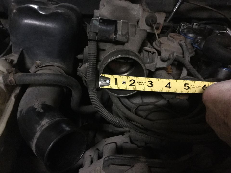 Close-up of a car engine's throttle body with a measuring tape showing 3 inches.