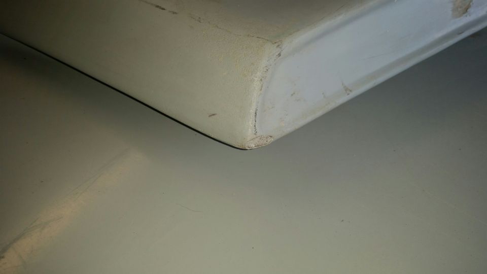 Close-up of a light-colored vehicle corner on a gray floor.